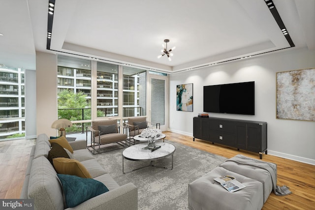 living area with a raised ceiling, baseboards, and wood finished floors