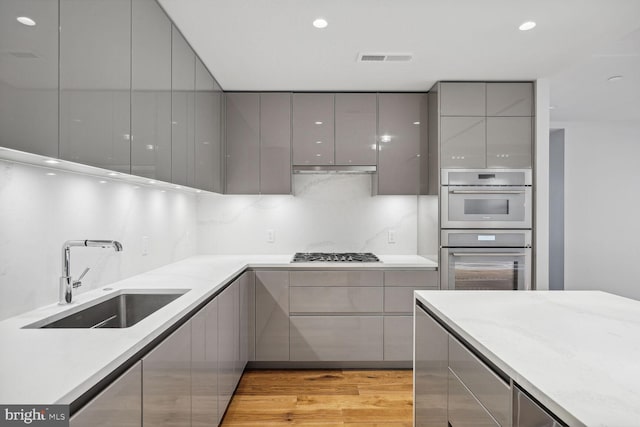 kitchen with light wood-style flooring, modern cabinets, stainless steel appliances, gray cabinetry, and a sink