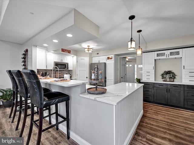 kitchen featuring light stone counters, backsplash, appliances with stainless steel finishes, dark wood-type flooring, and a peninsula