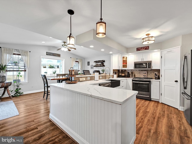 kitchen with lofted ceiling, backsplash, appliances with stainless steel finishes, wood finished floors, and a peninsula