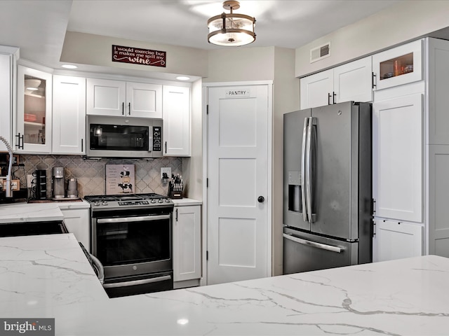 kitchen featuring stainless steel appliances, visible vents, white cabinets, light stone countertops, and tasteful backsplash