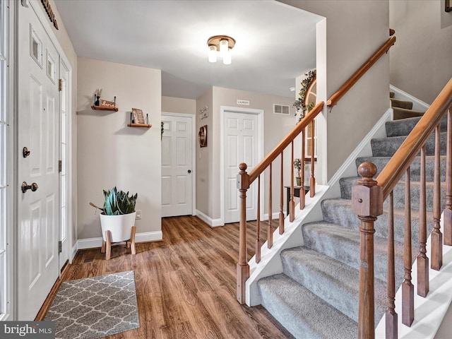 foyer entrance featuring visible vents, stairway, baseboards, and wood finished floors