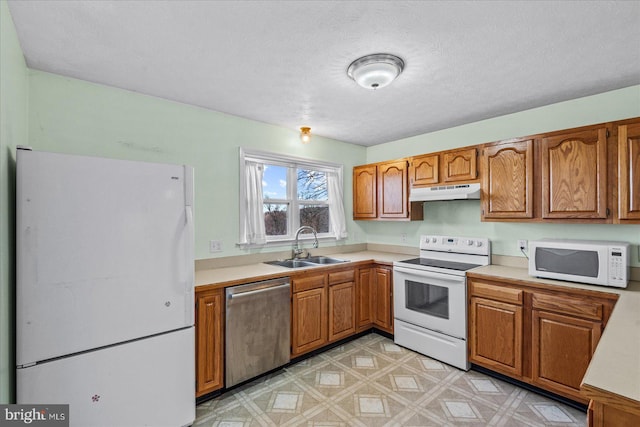 kitchen featuring under cabinet range hood, white appliances, a sink, light countertops, and light floors