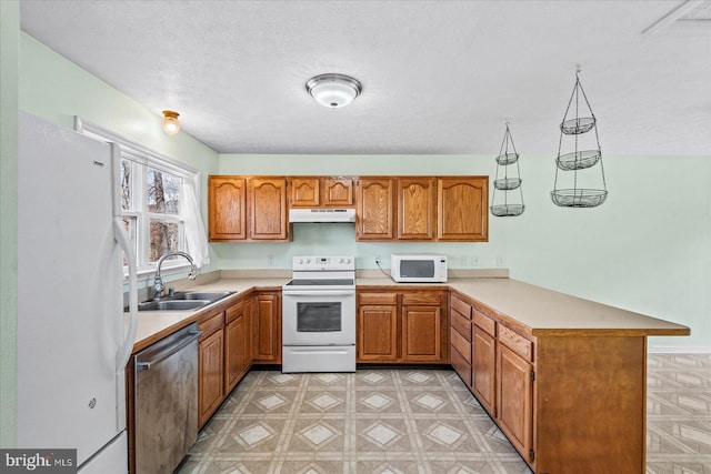 kitchen with under cabinet range hood, a peninsula, white appliances, a sink, and brown cabinetry