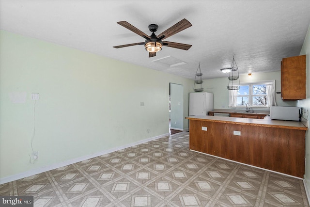 kitchen with a peninsula, a sink, baseboards, freestanding refrigerator, and light floors