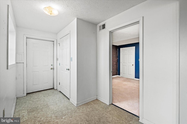 corridor featuring baseboards, carpet, visible vents, and a textured ceiling