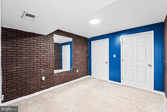 unfurnished bedroom featuring brick wall, a textured ceiling, visible vents, and carpet flooring