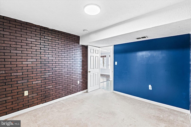 carpeted spare room with baseboards, visible vents, a textured ceiling, and brick wall