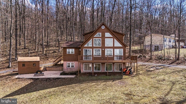 rear view of property featuring a storage shed, a deck, an outdoor structure, a fire pit, and stairs