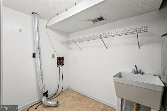 clothes washing area featuring hookup for a washing machine, visible vents, a sink, a textured ceiling, and baseboards