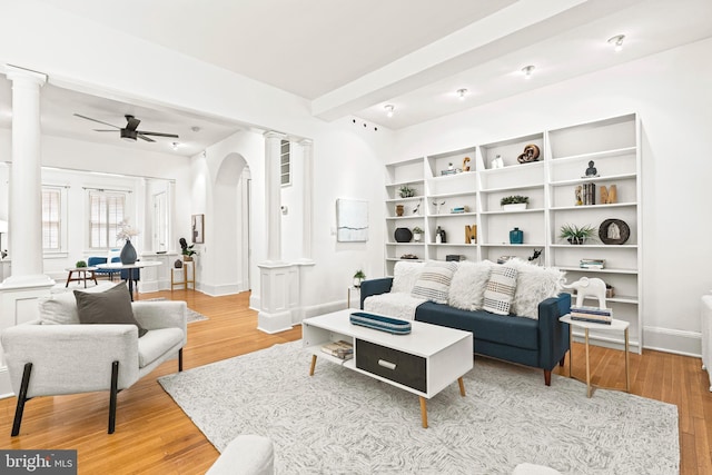 living room featuring arched walkways, a ceiling fan, light wood-style flooring, and ornate columns