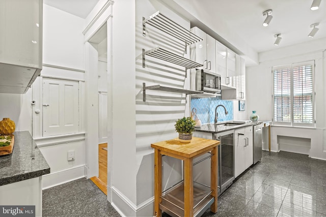 kitchen with stainless steel appliances, granite finish floor, a sink, baseboards, and white cabinets