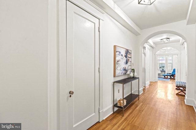 corridor featuring light wood-type flooring, arched walkways, and baseboards