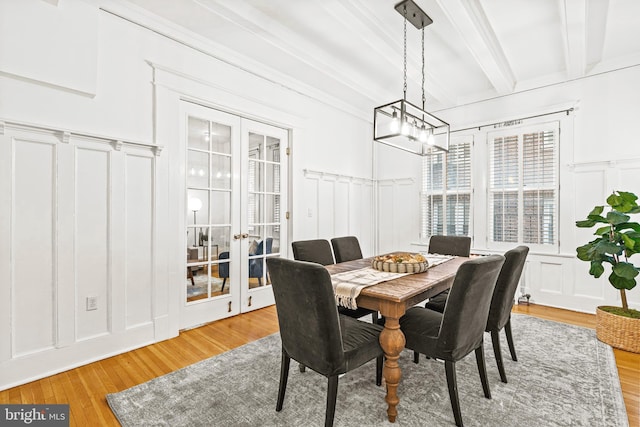 dining area with french doors, wood finished floors, beam ceiling, and a decorative wall