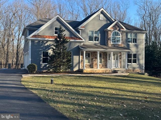 view of front of property featuring covered porch, stone siding, and a front yard