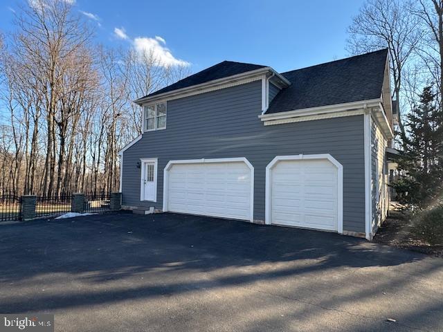 view of property exterior with fence, aphalt driveway, and roof with shingles