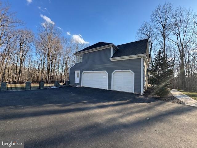 view of property exterior with a garage, aphalt driveway, and fence