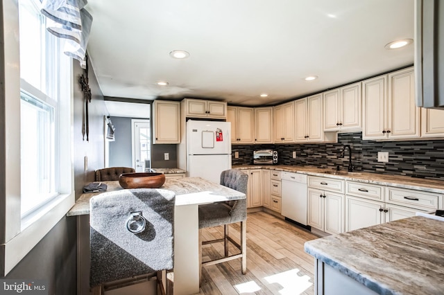 kitchen with white appliances, a sink, light wood finished floors, and decorative backsplash