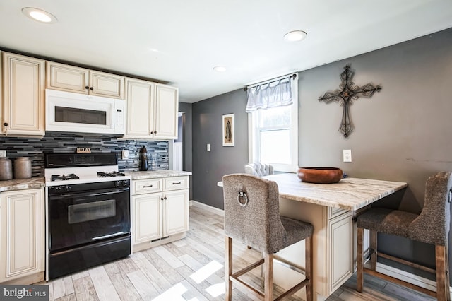 kitchen featuring white microwave, backsplash, light wood finished floors, gas range oven, and a kitchen bar