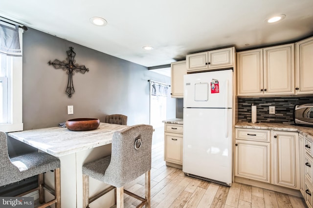 kitchen with recessed lighting, cream cabinetry, light wood-type flooring, freestanding refrigerator, and tasteful backsplash