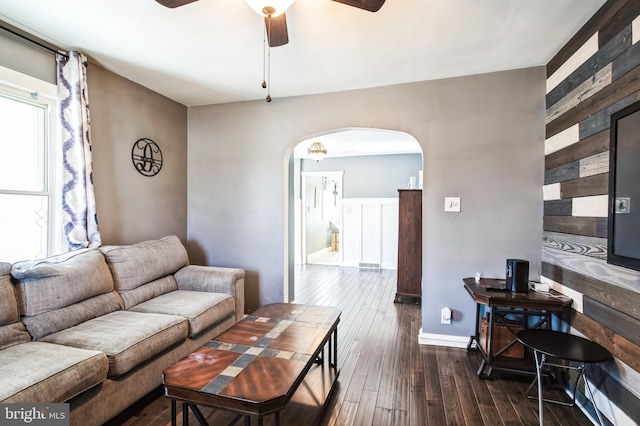 living room with a ceiling fan, arched walkways, and dark wood-type flooring