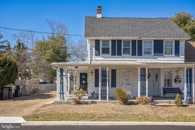 view of front facade with a porch, roof with shingles, fence, and a chimney