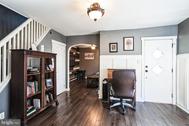 office space with dark wood-type flooring, arched walkways, a wainscoted wall, and a decorative wall