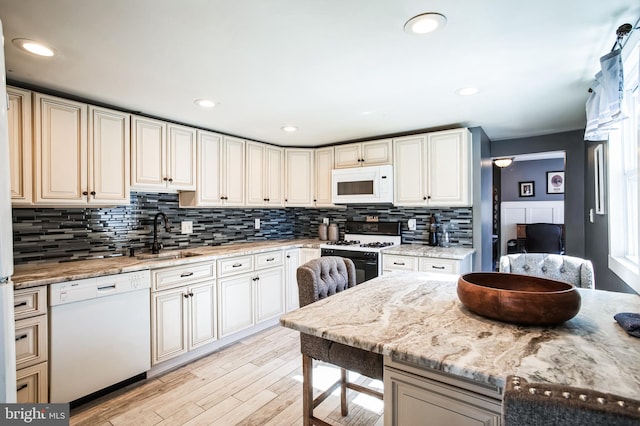 kitchen featuring light stone counters, light wood-style flooring, decorative backsplash, a sink, and white appliances