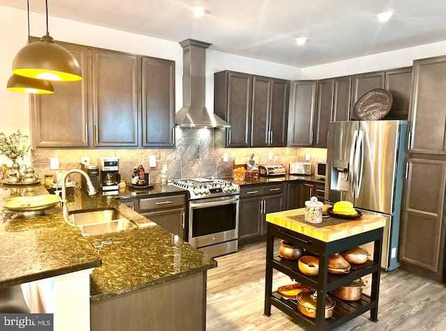 kitchen featuring dark stone countertops, a sink, appliances with stainless steel finishes, wall chimney range hood, and backsplash