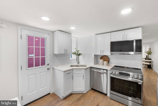 kitchen with backsplash, appliances with stainless steel finishes, light countertops, white cabinets, and light wood finished floors