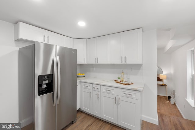 kitchen with white cabinets, light stone counters, light wood finished floors, baseboards, and stainless steel refrigerator with ice dispenser