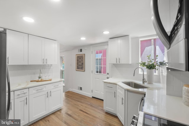 kitchen with backsplash, stainless steel refrigerator, a sink, baseboards, and white cabinetry