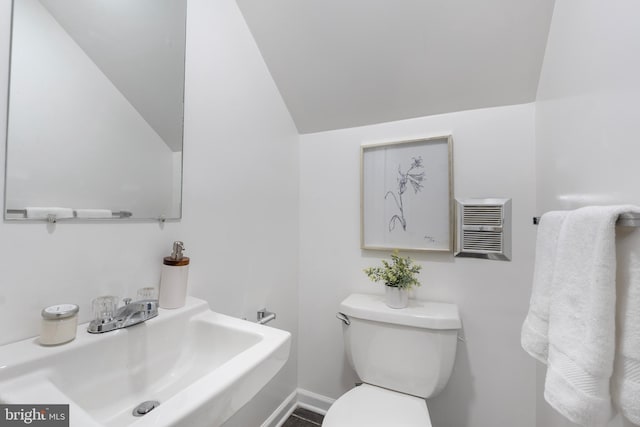 half bath with toilet, baseboards, vaulted ceiling, and a sink