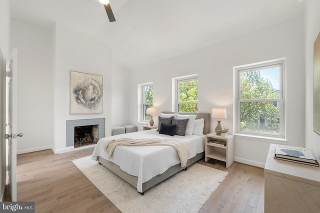 bedroom with a fireplace, light wood-style floors, a ceiling fan, baseboards, and lofted ceiling