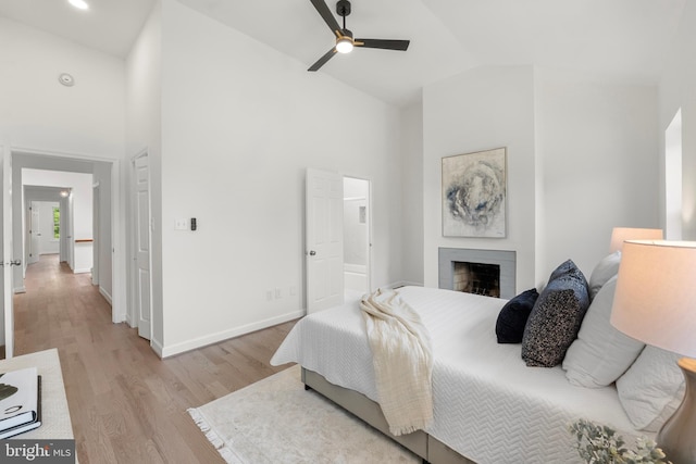 bedroom featuring baseboards, light wood finished floors, a fireplace, and high vaulted ceiling