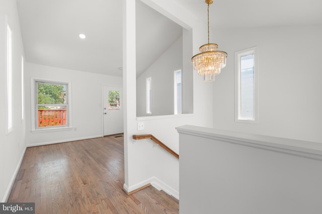 entryway featuring baseboards, a notable chandelier, wood finished floors, and vaulted ceiling