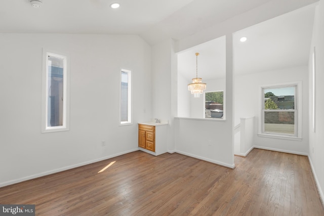 empty room with a chandelier, baseboards, vaulted ceiling, and wood finished floors
