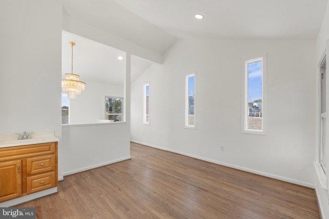 unfurnished living room with baseboards, a notable chandelier, light wood-type flooring, and lofted ceiling
