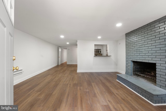 unfurnished living room with recessed lighting, a baseboard heating unit, wood finished floors, and a fireplace