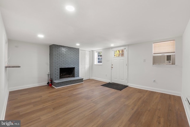 unfurnished living room featuring a brick fireplace, wood finished floors, baseboards, cooling unit, and recessed lighting