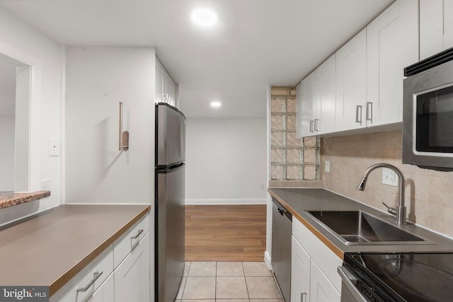 kitchen with backsplash, appliances with stainless steel finishes, white cabinetry, a sink, and light tile patterned flooring