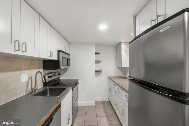 kitchen featuring appliances with stainless steel finishes, a sink, baseboards, white cabinets, and light tile patterned flooring