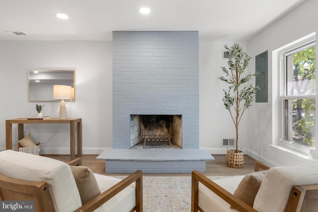 living room featuring electric panel, visible vents, a fireplace, wood finished floors, and baseboards
