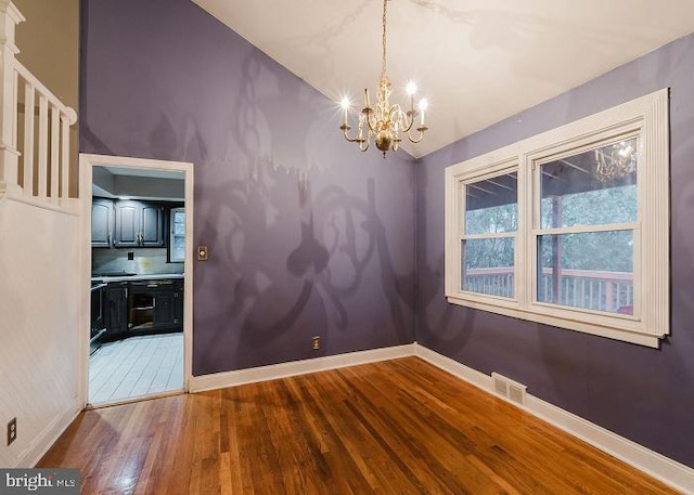 unfurnished dining area featuring visible vents, baseboards, lofted ceiling, wood-type flooring, and an inviting chandelier