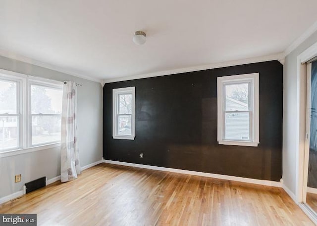 empty room with crown molding, wood finished floors, visible vents, and baseboards