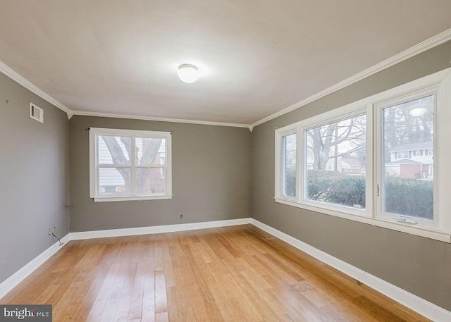 empty room featuring light wood finished floors, baseboards, visible vents, and ornamental molding