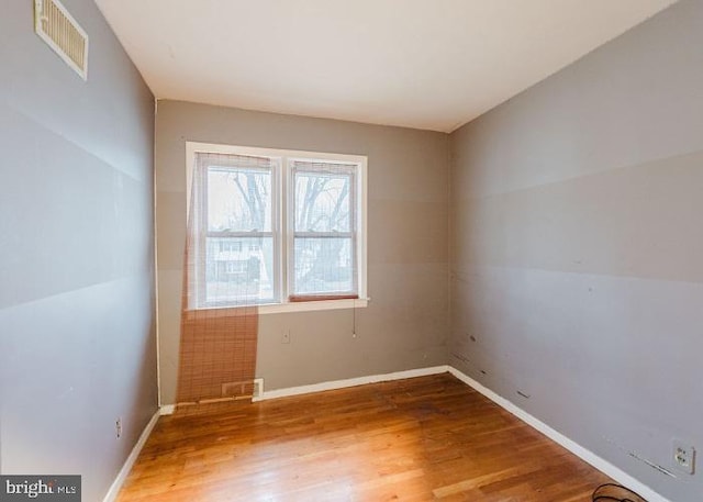 spare room with baseboards, visible vents, and wood finished floors