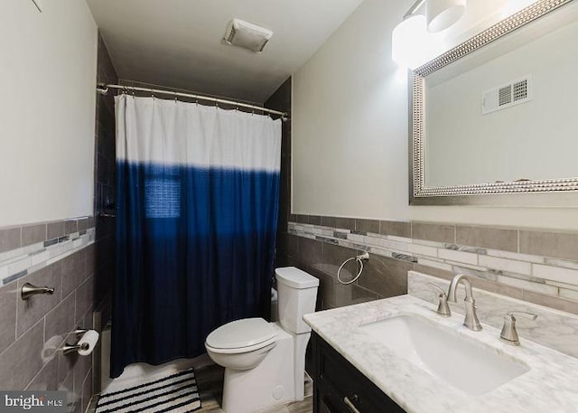 bathroom with a wainscoted wall, tile walls, visible vents, toilet, and vanity