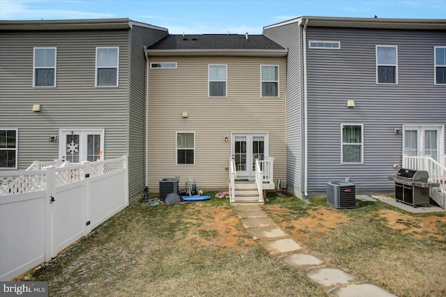 back of property featuring central air condition unit, fence private yard, and a lawn