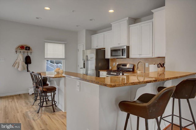 kitchen featuring white cabinets, light stone counters, stainless steel appliances, light wood-type flooring, and a kitchen bar